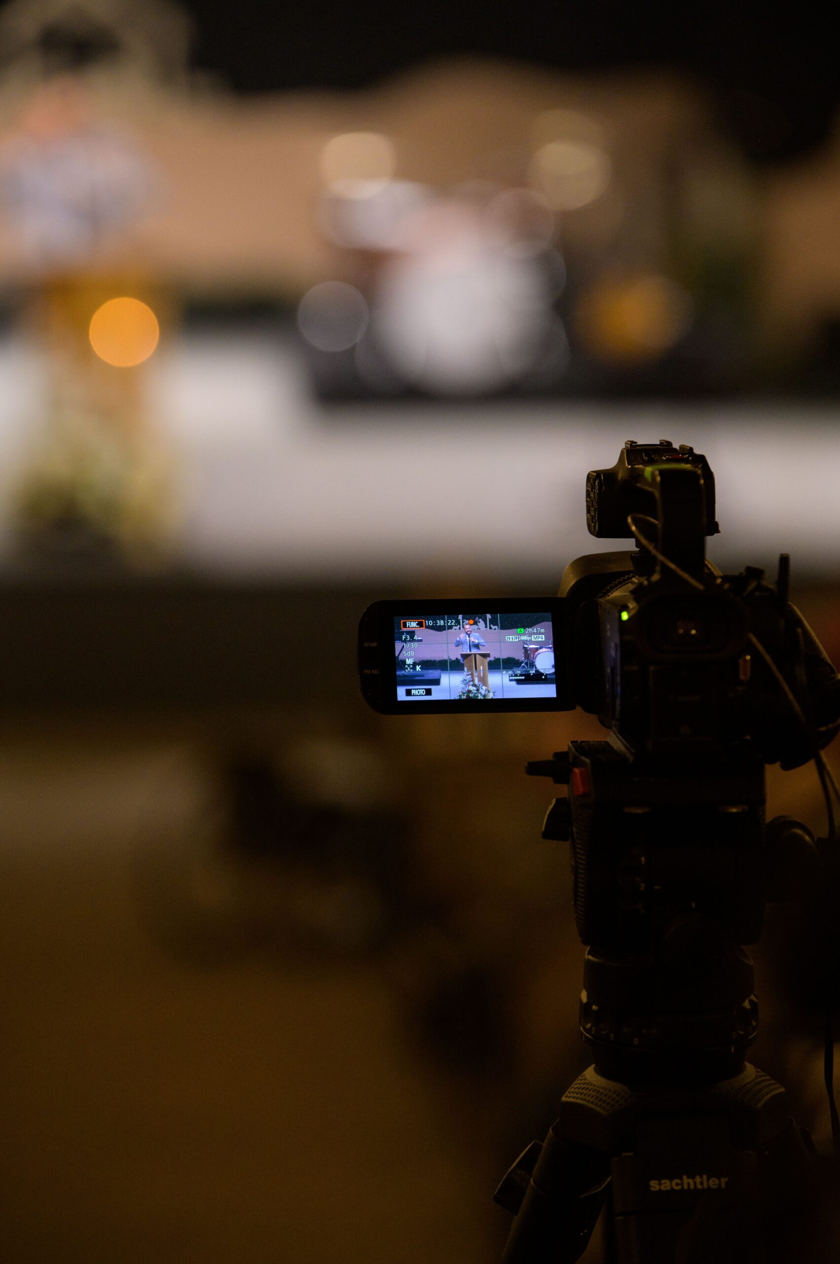 Close-up of a camera on a tripod recording a performance in a dimly lit studio setting.